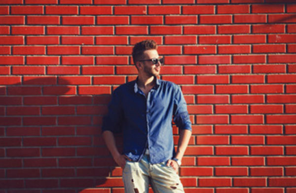 Харизматичный парень в солнцезащитных очках на фоне красной кирпичной стены
