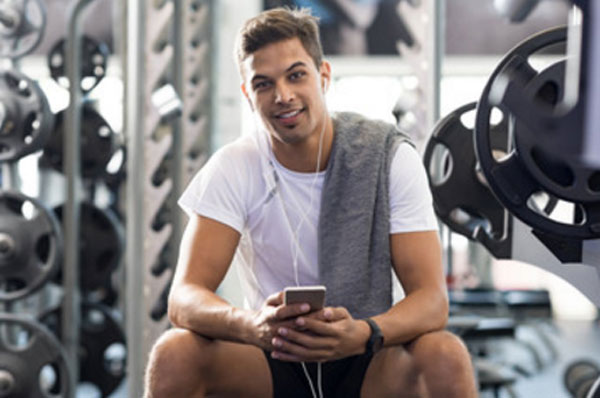 Счастливый парень с телефоном в руках сидит в тренажерном зале
