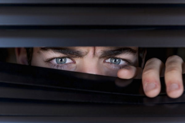 Мужчина выглядывает через щелочку в жалюзи