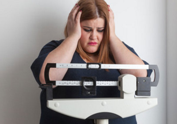 Полная женщина стоит на весах. Она с ужасом держится за голову