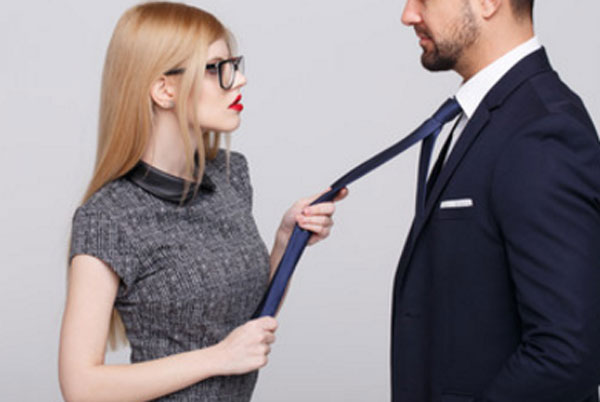 Девушка в очках держит парня в костюме за галстук