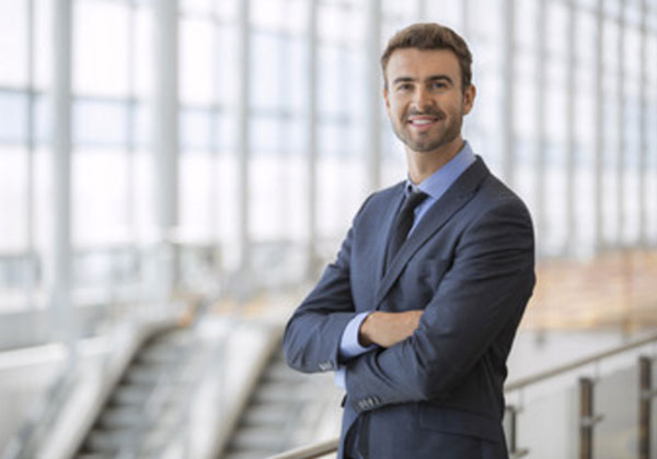 Улыбающийся мужчина стоит в костюме, сложив руки перед собой