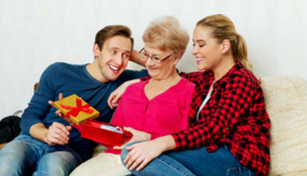 Муж, жена и мама мужа сидят на диване. Маме вручили подарки