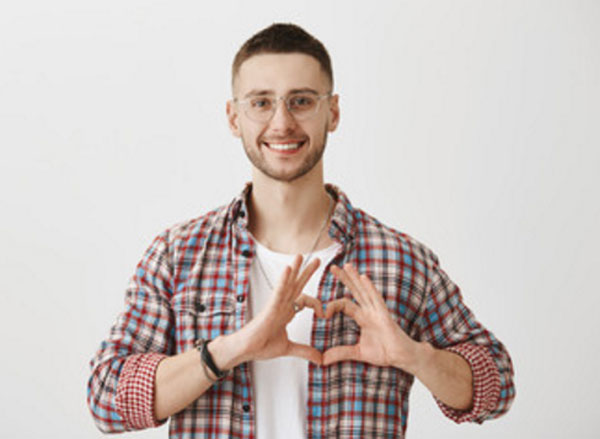 Парень в очках улыбается, он счастлив. Пальцами сделал форму сердца
