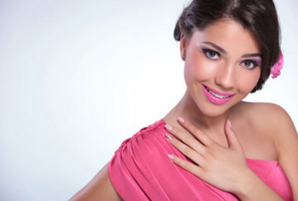 Улыбающаяся девушка в розовом платье с розовыми тенями, розовой помадой и розовым цветочком в волосах