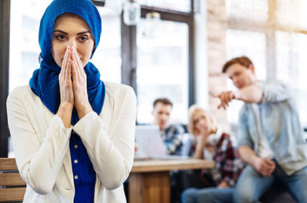 Мусульманка стоит на переднем плане. Сзади нее два парня и девушка. Один из парней тычет пальцем на мусульманку