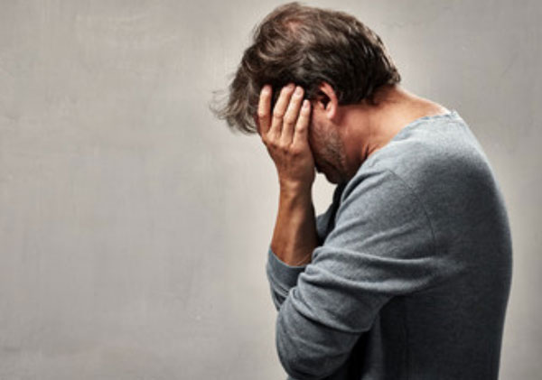 Расстроенный мужчина стоит с опущенной головой. Прячет глаза рукой