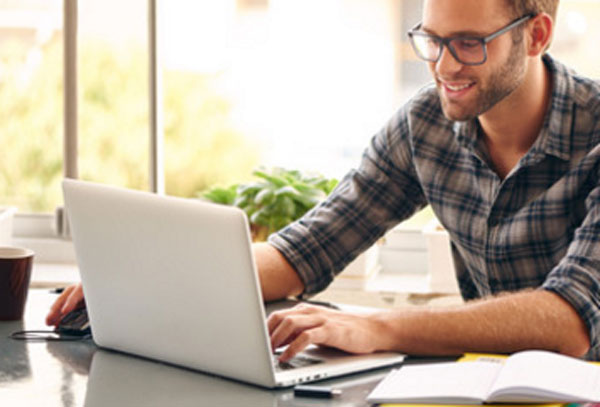 Парень улыбается. Он работает за ноутбуком