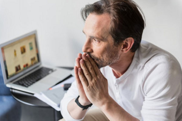 Расстроенный мужчина сидит возле включенного ноутбука