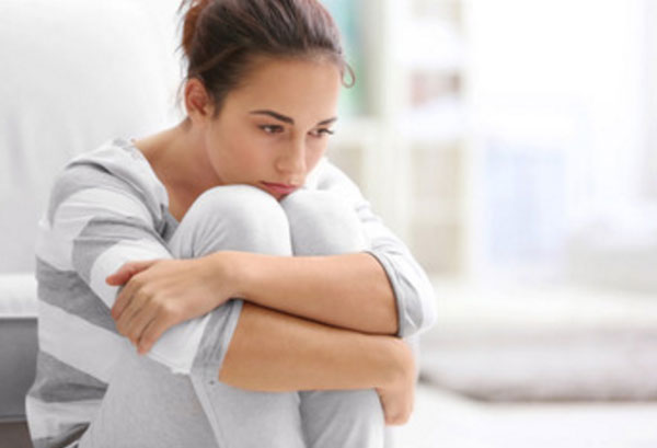 Расстроенная девушка сидит в задумчивости, поджав к себе ноги