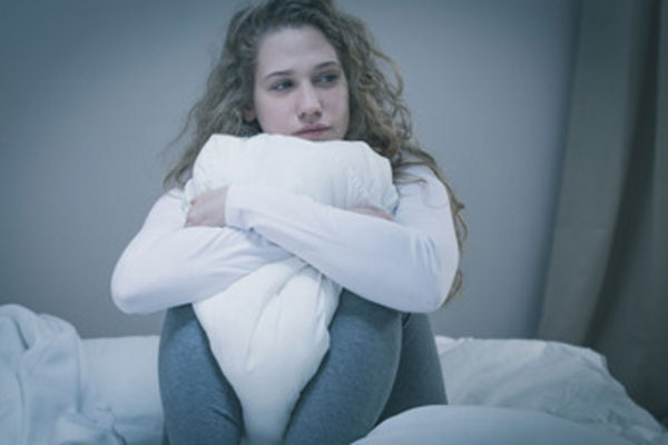 Грустная девушка сидит в обнимку с подушкой