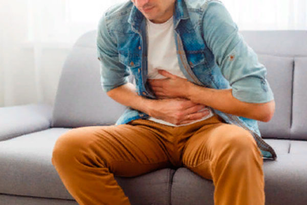 Мужчина сидит на диване и держится за живот