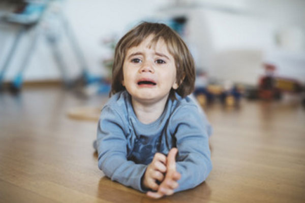 Мальчик лежит на животе на полу и хнычет