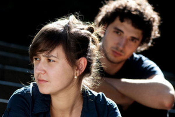 Девушка сидит впереди парня и смотрит в сторону.