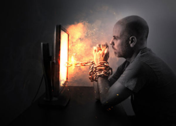 Мужчина сидит перед экраном монитора. Его руки скованы цепью