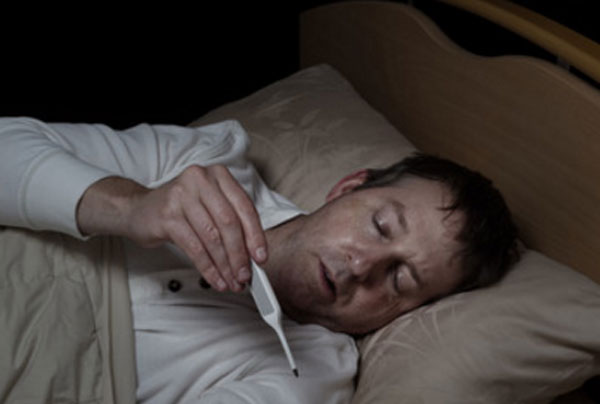 Больной мужчина в постели, смотрит на градусник