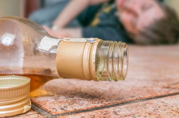 На переднем плане бутылка со спиртным, которая лежит на полу. На заднем - спящий мужчина