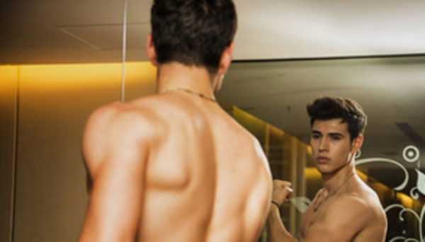 Парень стоит перед зеркалом и любуется своей привлекательностью