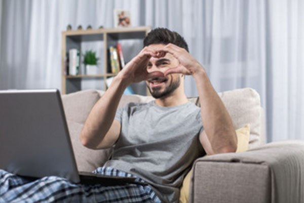 Парень сидит за ноутбуком. Руками показывает сердечко