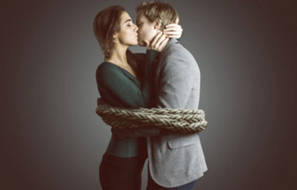 Мужчина и женщина обнимают друг друга и целуют. Они связаны толстой веревкой