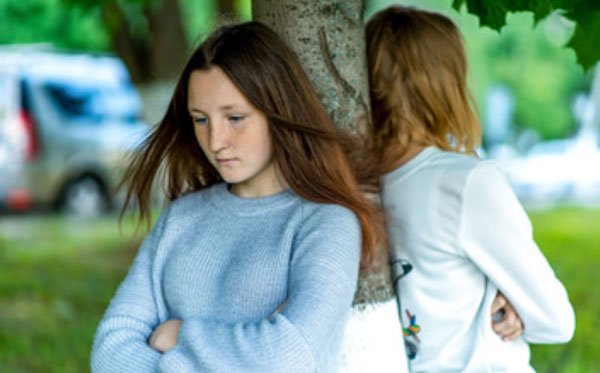 Две девушки стоят возле дерева спинами друг к другу