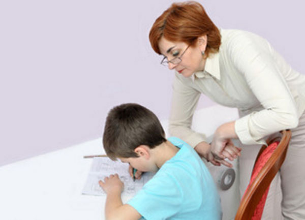 Мама стоит над сыном, следит, что он пишет