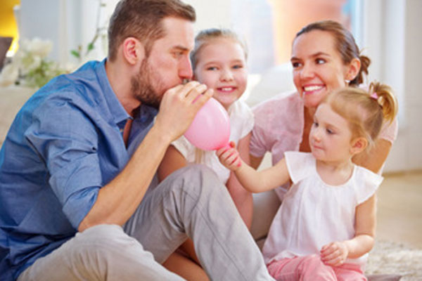 Папа надувает шарик, рядом дочки и жена