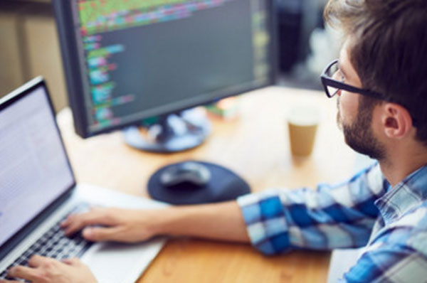 Парень что-то печатает на ноутбуке. На мониторе компьютера напечатаны коды