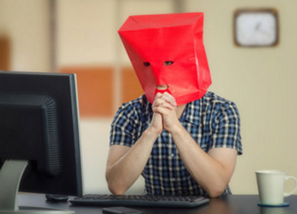 Мужчина сидит перед компьютером в картоном пакете с прорезями для глаз