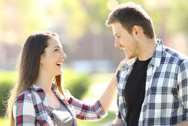 Девушка касается плеча парня и смеется. Парень улыбается