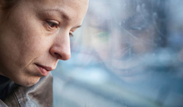 Женщина с отрешенным взглядом облокотила голову на стекло окна