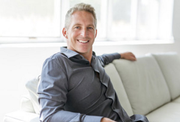 Красивый, улыбающийся мужчина 40 лет сидит на диване