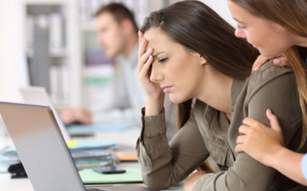 Расстроенная девушка сидит за ноутбуком, коллега пытается ее успокоить