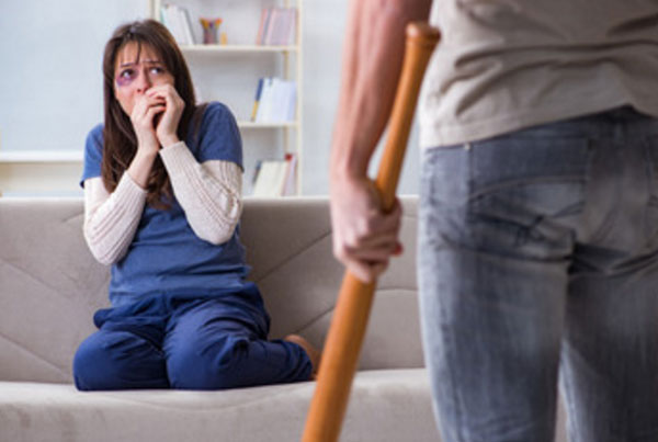 На диване сидит перепуганная жена с синяком под глазом. К ней приближается мужчина с битой в руках