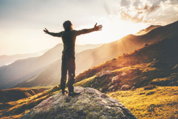 Мужчина стоит на склоне горы с распростертыми руками