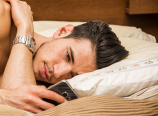 Грустный парень лежит в кровати и смотрит на свой телефон