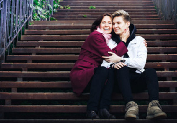 Парень с мамой сидит на ступеньках. Она его обнимает