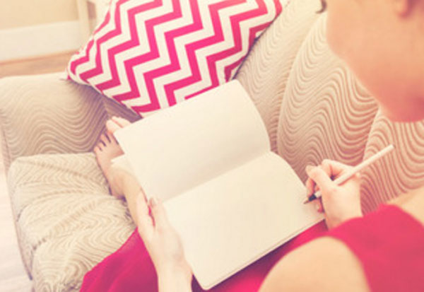 женщина сидит на диване и собирается что-то написать в блокноте