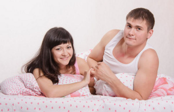 Мужчина и женщина в кровати, лежат на животе и улыбаются