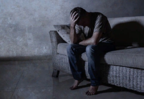 Расстроенный мужчина сидит на кровати с опущенной вниз головой