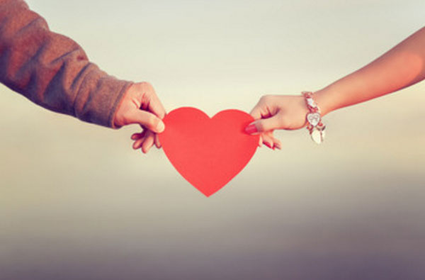 Женская и мужская рука с разных сторон держатся за бумажное сердце