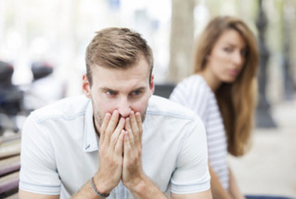 Парень сидит на скамейке в задумчивости и тревожности. На заднем плане сидит девушка