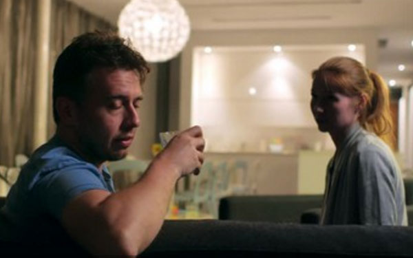 Женщина сидит рядом с мужем на диване. У него в руках стакан спиртного