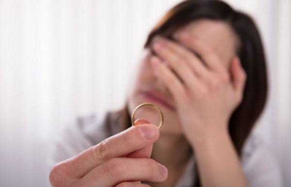 Женщина держит обручальное кольцо. Лицо закрыла руками