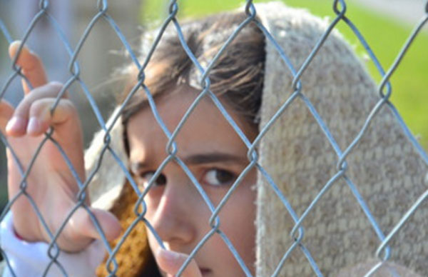Напуганная девочка смотрит через прутья забора