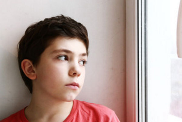 Мальчик сидит у окна и грустно в него смотрит