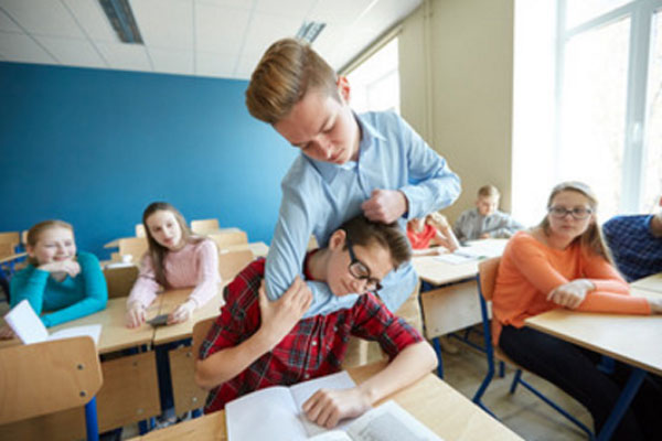 Один ученик схватил за голову другого, сидящего за партой