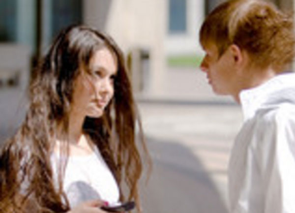 Парень стоит близко с девушкой. Она смотрит на него