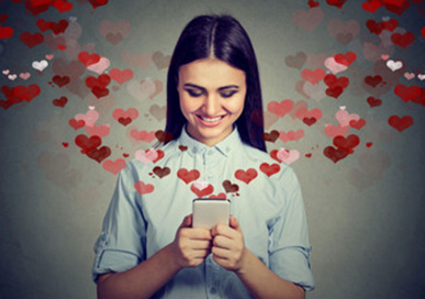 Девушка улыбается. Она смотрит на телефон, а с него вылетают сердечки