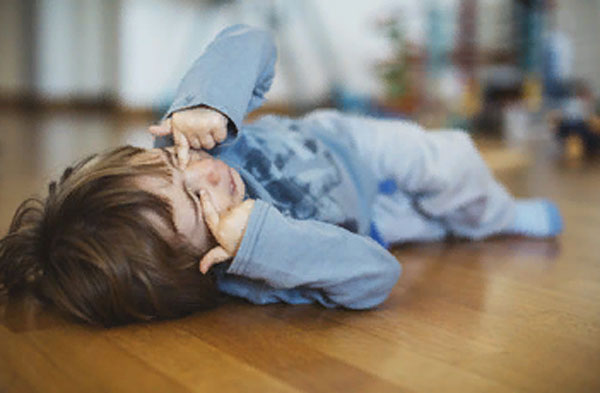 Ребенок лежит на полу и трет заплаканные глаза